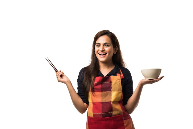 Indian Woman chef wearing apron and holding empty ceramic dinner plate and bowl with different  facial expressions standing isolated over white background