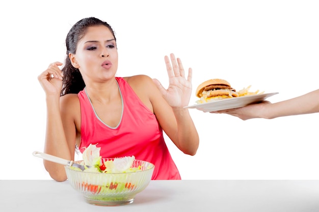 건강한 샐러드를 먹고 흰색 배경에 고립된 햄버거를 거부하는 인도 여성