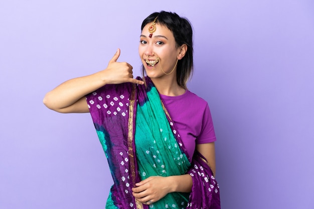 Indian woman isolated on purple making phone gesture. call me back sign