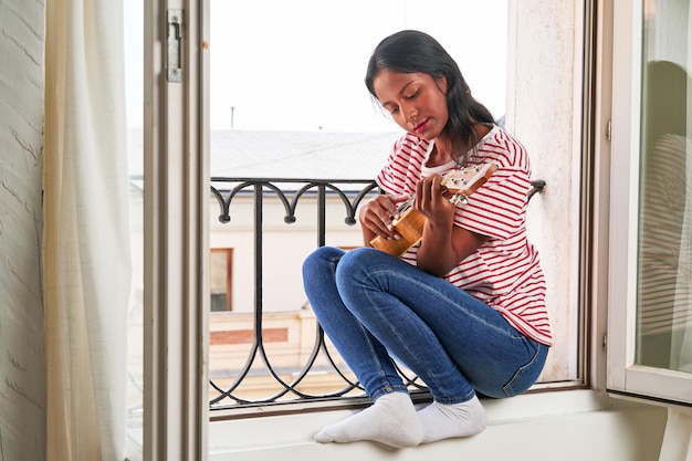 Indian woman playing ukulele on windowsill