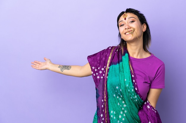 Indian woman on purple wall extending hands to the side for inviting to come