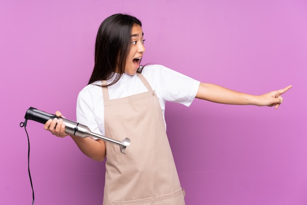 Indian woman using hand blender isolated on purple pointing finger to the side