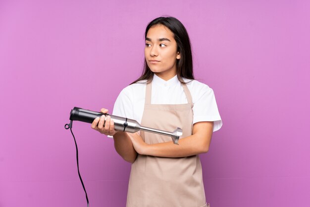 Indian woman using hand blender on purple looking side