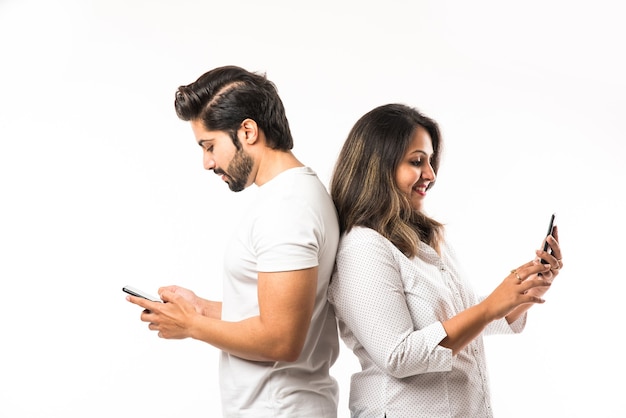 Indian young couple using smartphone or mobile handset, standing isolated over white background or against red brick background