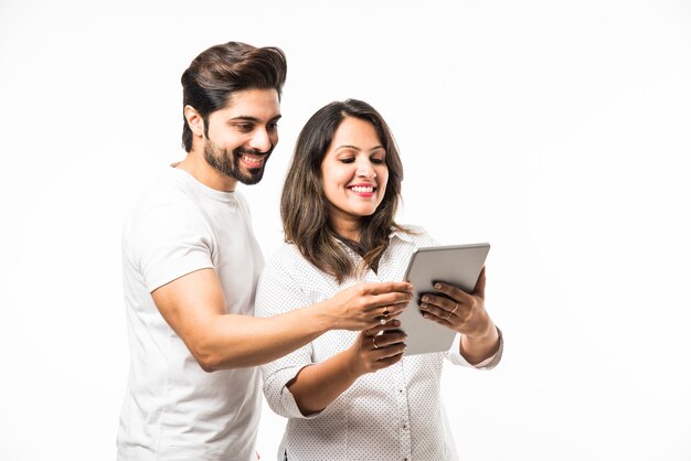 Indian young couple using smartphone or mobile handset, standing isolated over white background or against red brick background