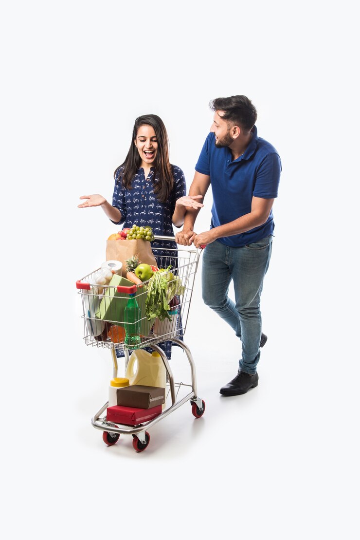 Photo indian young couple with shopping cart or trolly full of grocery, vegetables and fruits.  isolated full length photo over white wall