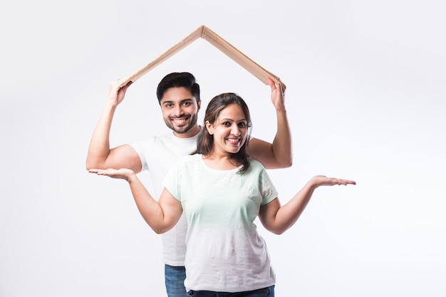 Индийская молодая семейная пара и концепция недвижимости - покупка или аренда, стоя на белом фоне