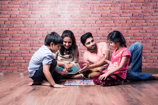 Indian young family of four playing board games like Chess, Ludo or Snack and Ladder at home in quarantine