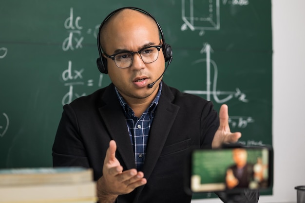 Indian young teacher man sitting wearing headset teaching online video conference smartphone