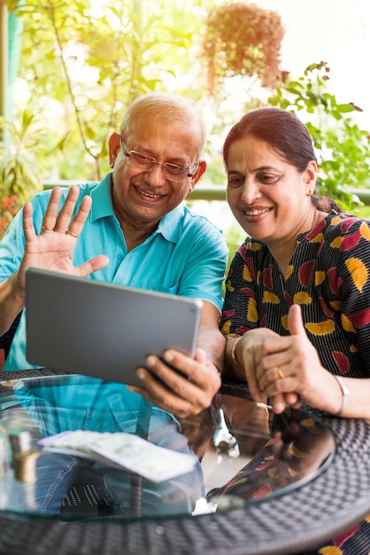 Indiase Aziatische Senior paar videochatten op tabletcomputer zittend op de bank of in de tuin thuis, selectieve focus