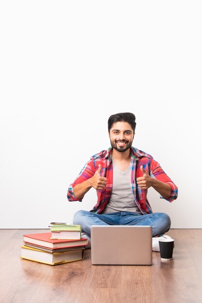 Indiase Aziatische universiteit of hogeschool student zitten met laptopcomputer met boeken op houten vloer tegen witte achtergrond