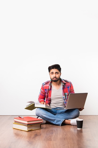 Indiase Aziatische universiteit of hogeschool student zitten met laptopcomputer met boeken op houten vloer tegen witte achtergrond