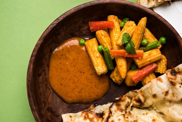 Indiase baby corn masala curry bereid in rode saus geserveerd met roti/ naan of indiaas brood. over humeurige achtergrond. selectieve focus