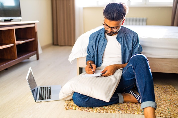 Indiase bebaarde man zittend op de vloer en het maken van financiële berekeningen online zaken in nieuw appartement