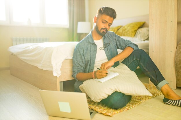 Indiase bebaarde man zittend op de vloer en het maken van financiële berekeningen online zaken in nieuw appartement
