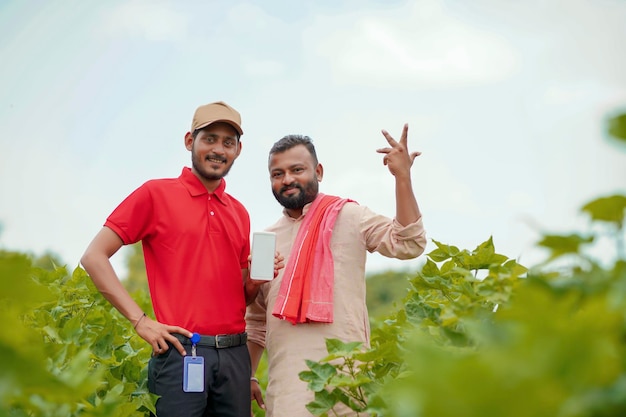 Indiase boer die smartphone toont met agronoom of officier op landbouwveld.