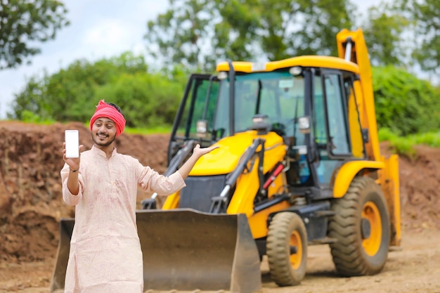 Indiase boer die smartphone toont met zijn nieuwe uitrusting voor grondverzetmachines