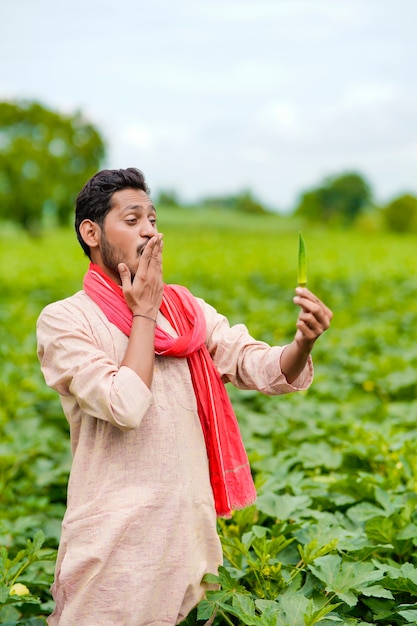 Indiase boer staat en houdt ladyfinger in de hand op landbouwveld.