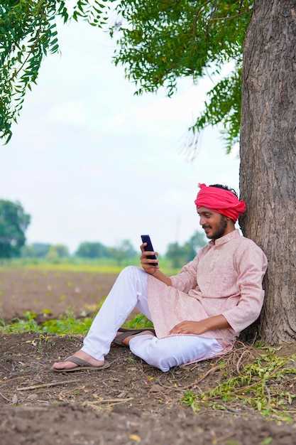 Indiase boer zit op landbouwveld en gebruikt smartphone.