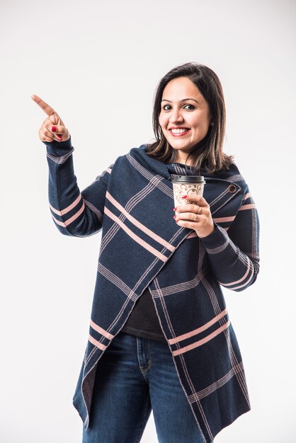 Indiase dame of vrouw in de winter draagt of drinkt warme koffie of thee in een draagbeker, staande geïsoleerd op een witte achtergrond