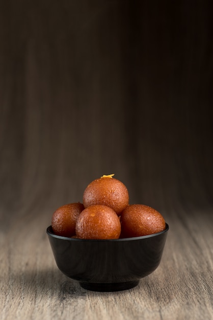 Foto indiase dessert of zoete schotel: gulab jamun in kom op houten achtergrond.