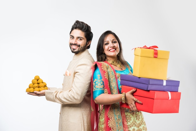 Indiase echtpaar met laddu en geschenkdozen op diwali of festival, staande geïsoleerd op een witte achtergrond. traditionele kleding dragen