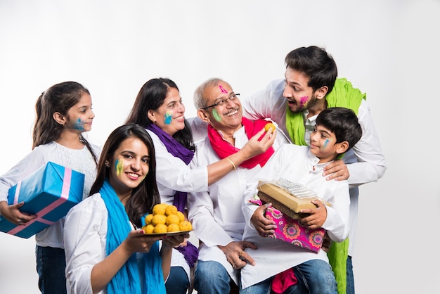 Indiase familie die holi-festival viert met zoete laddu-geschenken en kleuren in plaat. geïsoleerd op witte achtergrond. selectieve focus betekenis