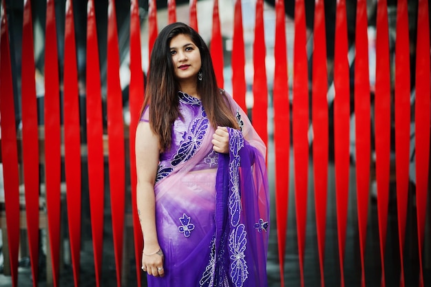 Indiase hindoe meisje op traditionele violet saree geposeerd op straat tegen rode achtergrond