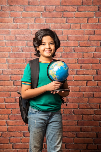 Indiase jongen met educatieve wereldbol, geïsoleerd op rode bakstenen muur. Nieuwsgierig mannelijk kind met aarde rond model in zijn hand. Kleine reiziger, nieuwe horizonten verkennen