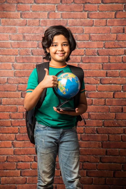 Indiase jongen met educatieve wereldbol, geïsoleerd op rode bakstenen muur. Nieuwsgierig mannelijk kind met aarde rond model in zijn hand. Kleine reiziger, nieuwe horizonten verkennen