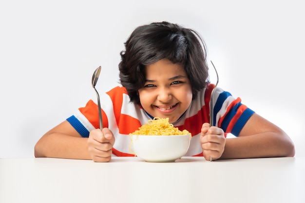 Indiase kind eet heerlijke noedels met vork tegen witte achtergrond, Aziatische jongen eet spaghetti in een kom tegen witte achtergrond