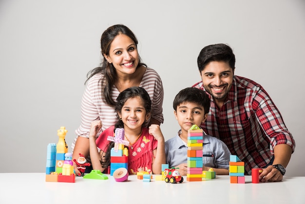 Indiase kleine kinderen die kleurrijk blokspeelgoed spelen met jonge ouders, tegen een witte achtergrond