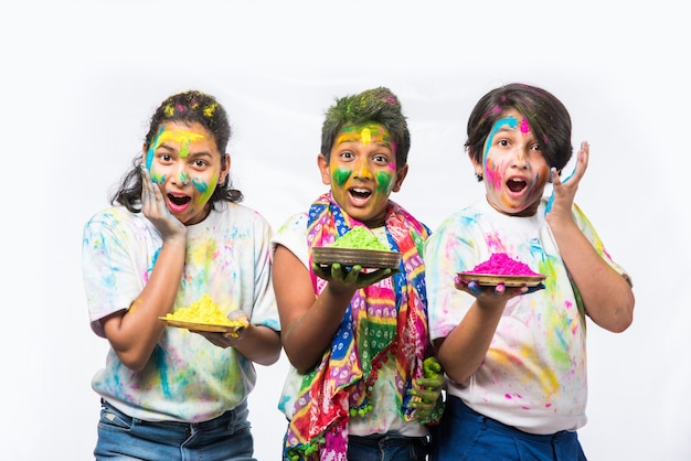 Indiase kleine kinderen of vrienden of broers en zussen die Holi-festival vieren met gulal of poederkleur, snoep, pichkari of spray, geïsoleerd op witte achtergrond