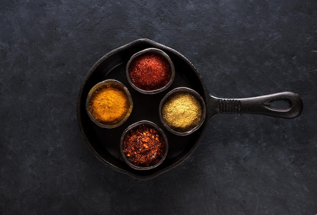 Indiase kruiden en pittig in kommen in een gietijzeren pan op een zwarte betonnen achtergrond bovenaanzicht Kurkuma chili koriander garam masala en paprika in kommen