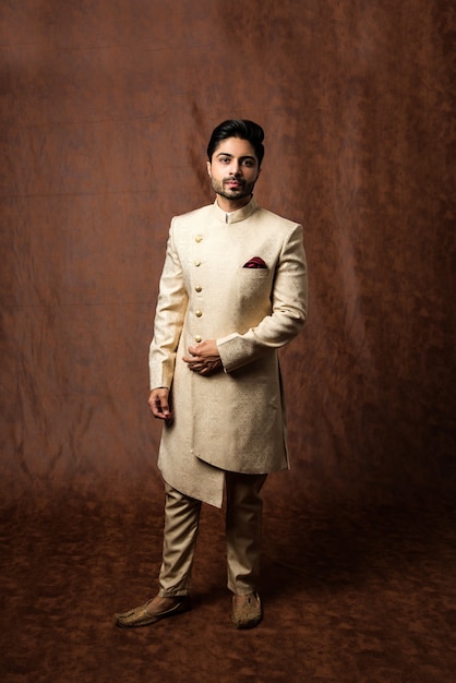 Indiase man in traditionele kleding OF kurta, pyjamadoeken. Mannelijke mannequin in sherwani, poseren of staan tegen bruine grunge achtergrond, selectieve focus