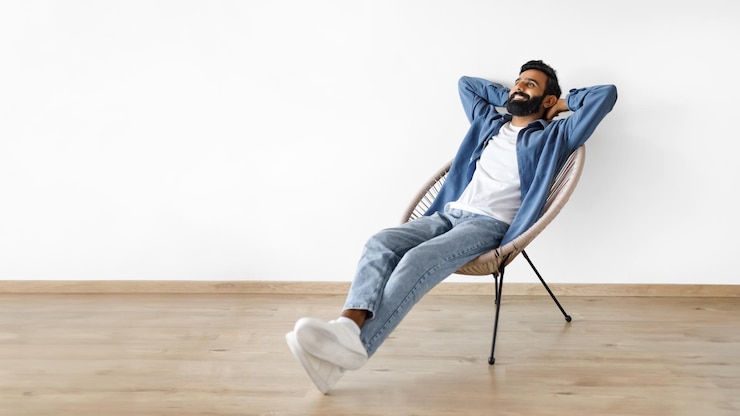 Foto indiase man ontspannen met handen achter hoofd in fauteuil binnen