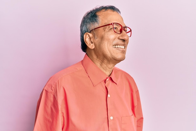 Indiase man van middelbare leeftijd met vrijetijdskleding en bril wegkijkend naar de zijkant met een glimlach op het gezicht natuurlijke uitdrukking zelfverzekerd lachend