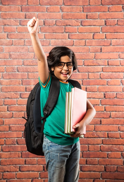 Indiase mannelijke jongen student met bril met notitieboekjes en schooltas tegen rode bakstenen muur