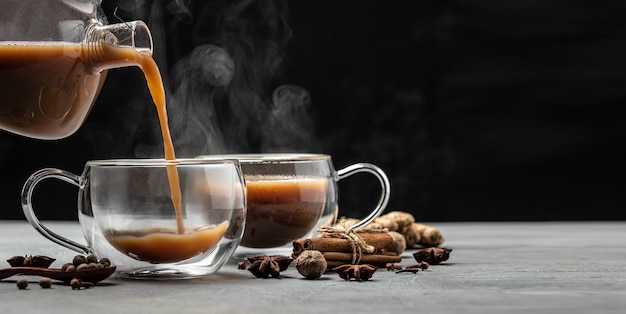 Indiase masala chai thee Hete masala chai gekruide thee met melk en kruiden wordt gegoten in een glas glas op donkere achtergrond Lange banner formaat plaats voor tekst