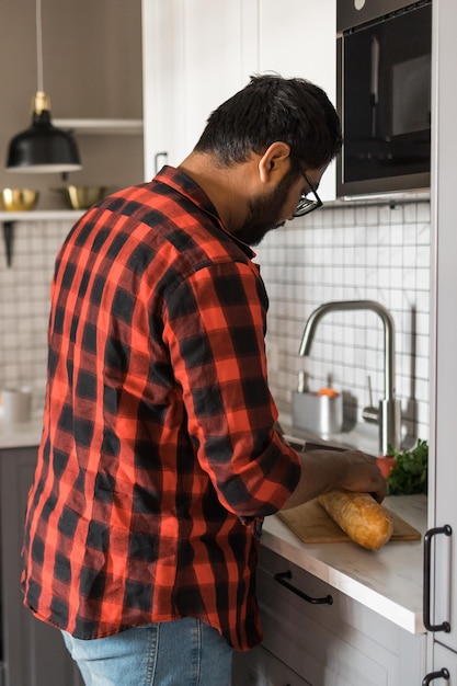 Indiase of latino man die ontbijt kookt terwijl hij in de keuken thuis achteraanzicht staat