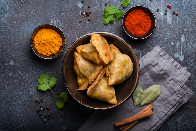 Indiase samosa's - gebakken/gebakken gebak met hartige vulling, populaire Indiase snacks, geserveerd in kom met kruiden en verse koriander op rustieke achtergrond, bovenaanzicht. Overhead van samosa's