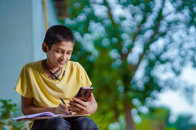 Indiase schooljongen met telefoonles op afstand met behulp van mobiele applicatie, online les kijken, videobellen in app maken van aantekeningen thuis studeren