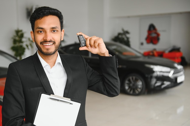 Indiase vrolijke autoverkoper die nieuwe auto laat zien in de showroom