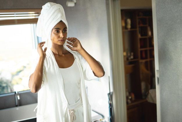 Indiase vrouw die handdoekverpakking aanpast op haar haar in een heldere badkamer met badjas en blinds