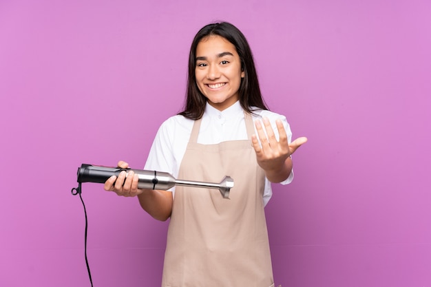 Indiase vrouw met behulp van handmixer geïsoleerd op paarse achtergrond uitnodigen om te komen