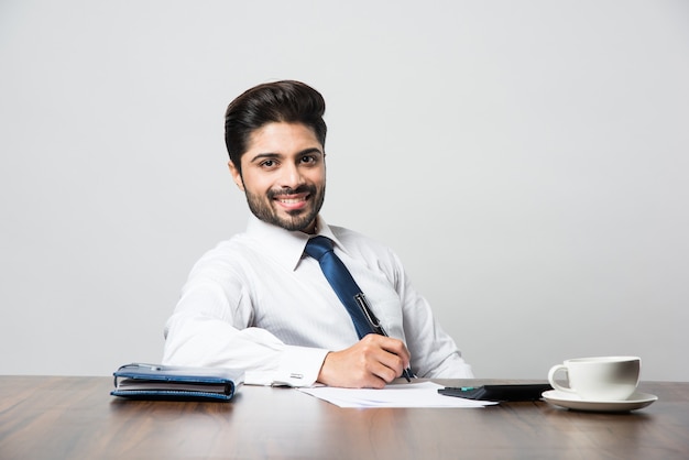 Indiase zakenman die een document schrijft terwijl hij aan een bureau of werkstation zit