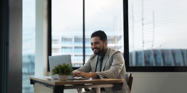 Indiase zakenman die laptop gebruikt tijdens het analyseren van rapporten op kantoor