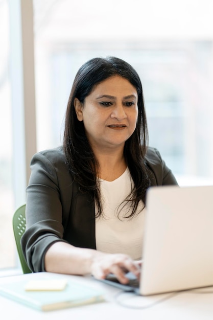 Indiase zakenvrouw die een laptop gebruikt die op een toetsenbord typt en online werkt in een modern kantoor