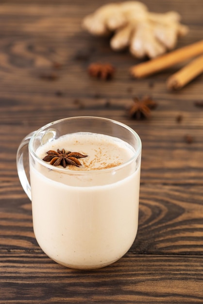 Indiase zelfgemaakte masala chai met melk en kruiden in een glazen mok op een houten tafel