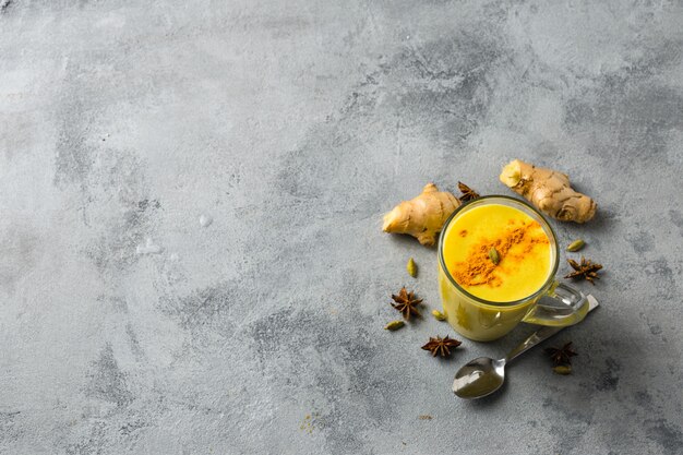 Foto indiër drinkt kurkuma gouden melk in glas. gouden latte met ingrediënten voor het koken.